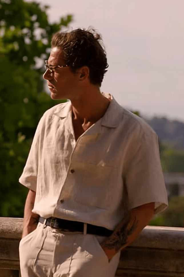 Herr-im-beigen-Leinenhemd-und-Sonnenbrille-steht-an-Brüstung-vintage-sommerlicher-Stil